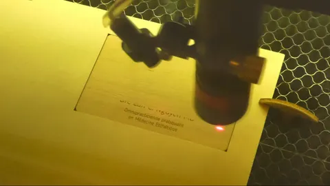 CO2 laser engraving an intricate wooden business card with a custom QR code on a honeycomb workbench.