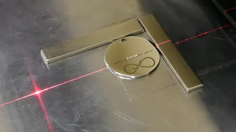 Industrial fiber laser engraving detailed custom typography and graphics onto round and heart-shaped metal charms.