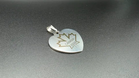Laser engraved stainless steel heart pendant featuring a precise Canadian maple leaf design and 2026 date.