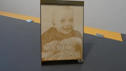 Laser engraved wood photo portrait of a smiling baby titled Maxim 2026 displayed inside a metal frame.