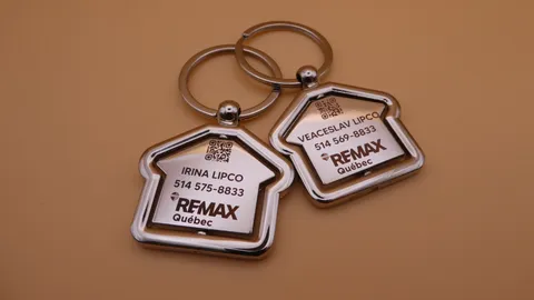 Double-sided 360-degree rotating house keychain with custom laser-engraved RE/MAX Québec branding, agent contact info, and QR code. Personalized real estate closing gift by TechArt Concept.