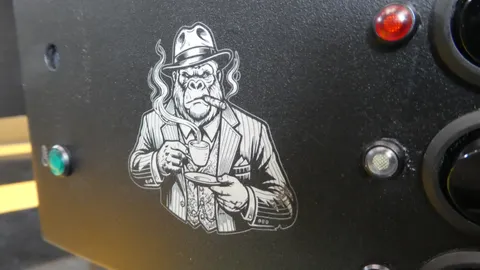 Angled view of a custom laser etched gorilla illustration on a black metal machinery faceplate beside an indicator light.