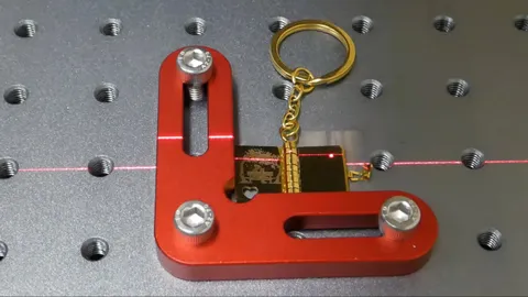 Close-up video of a fiber laser engraving intricate text and tiny details onto a miniature metal book keychain. A personalized sentimental gift from a mother to her children, handcrafted with industrial precision by TechArt Concept.